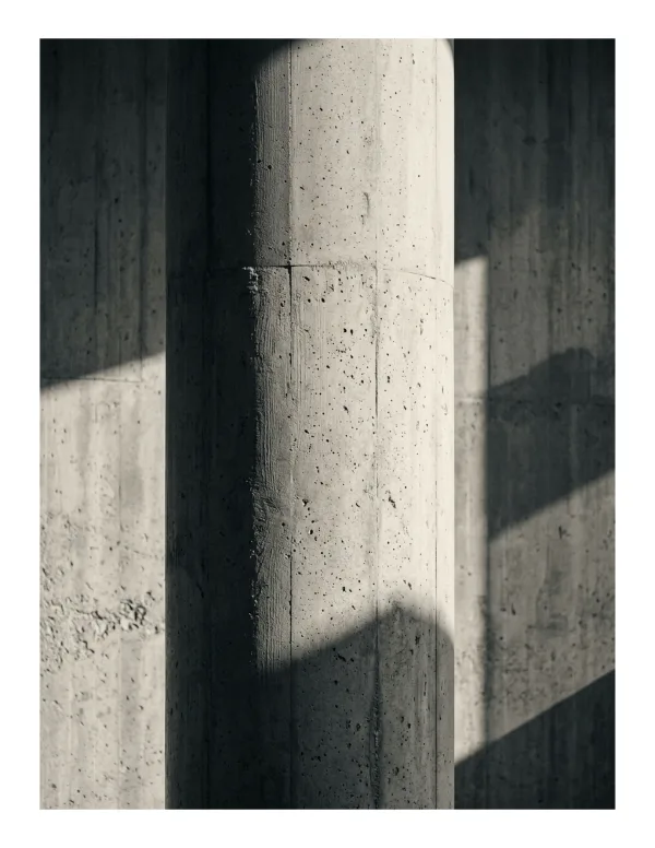 Close-up of a textured concrete column with strong shadows cast on the wall behind it.